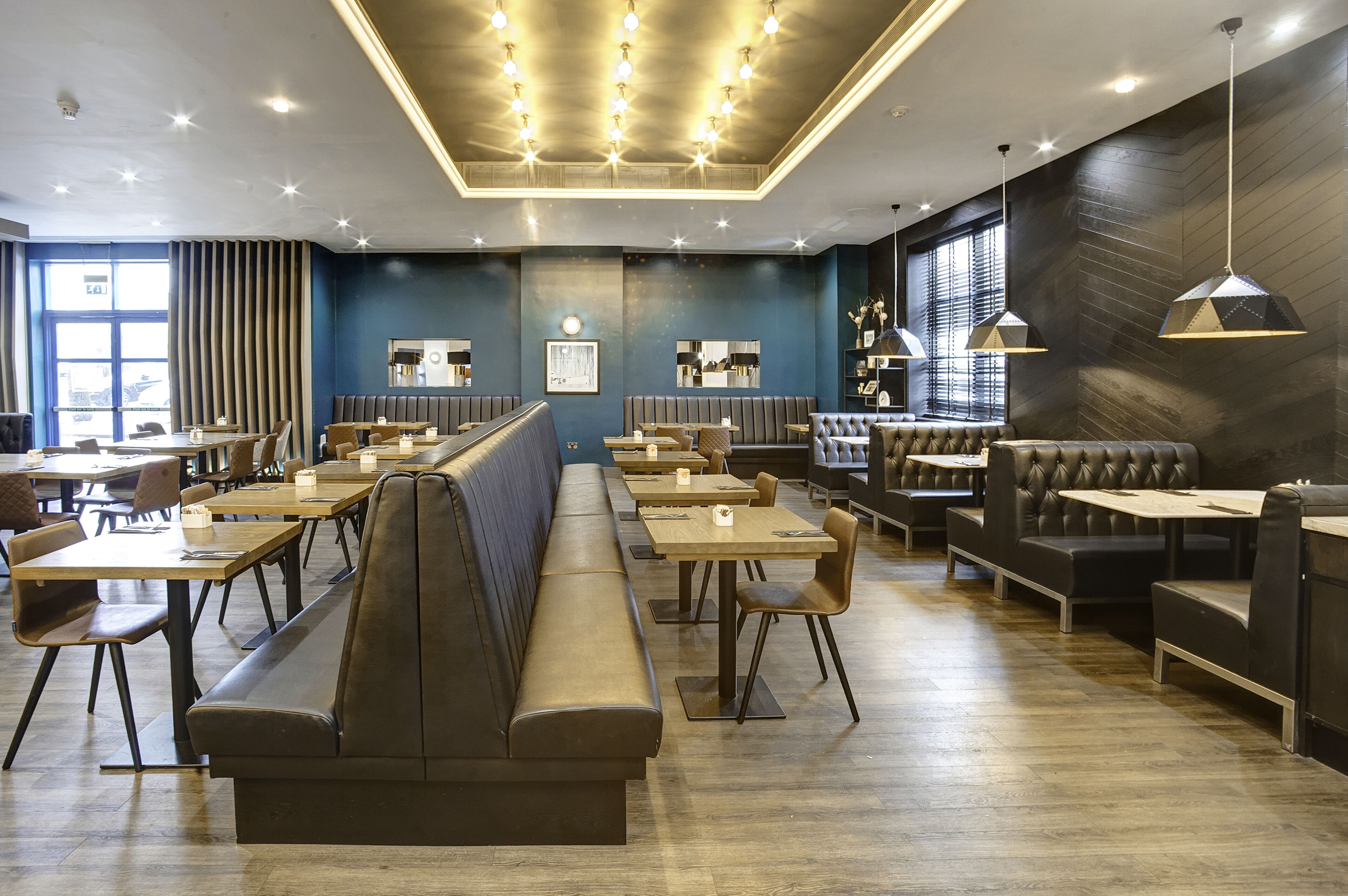 A modern restaurant with long booths, wooden tables, and pendant lighting.