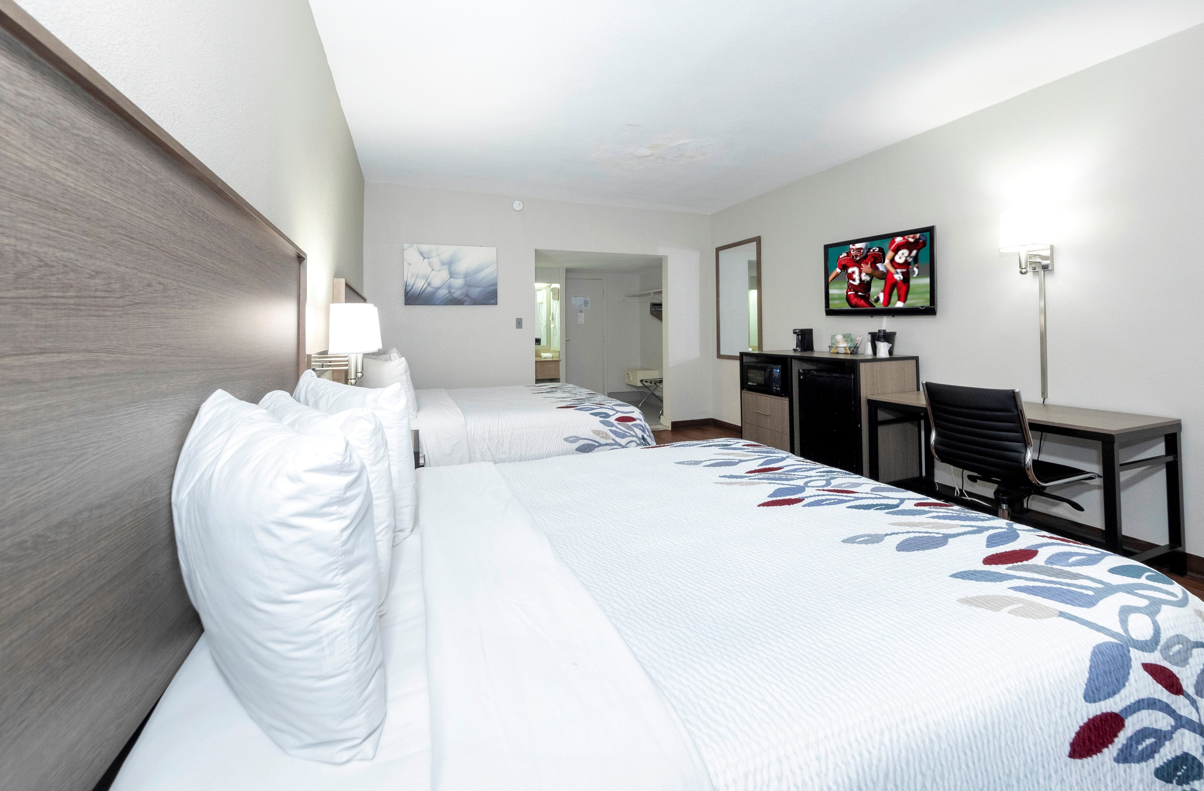 Ett hotellrum med två sängar, ett skrivbord, en stol, en tv och en spegel.