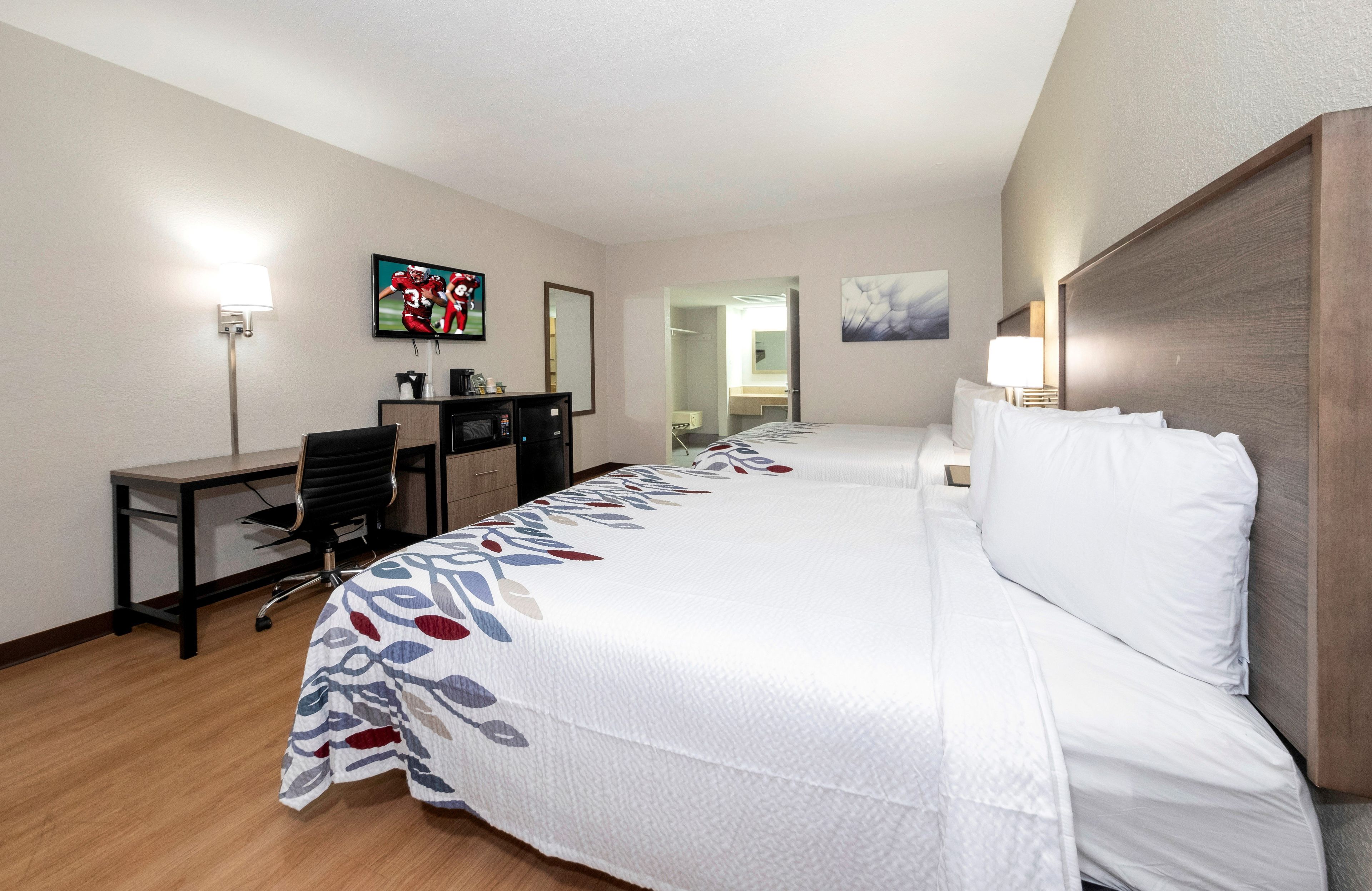 A hotel room with a bed, desk, chair, television, and a bathroom visible through an open door.