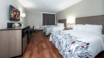 A hotel room with a desk, a television, a bed, and a window with curtains.