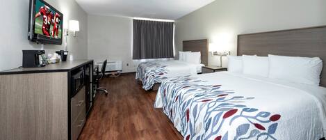 A hotel room with a desk, a television, a bed, and a window with curtains.