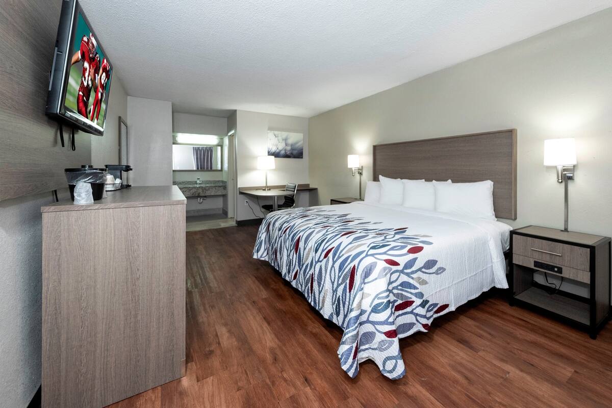 Camera d'albergo con un letto, comodini, una scrivania, una televisione e un bagno visibile attraverso una porta aperta.