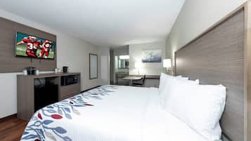 Quarto de hotel com cama, televisão, escrivaninha e uma cadeira.