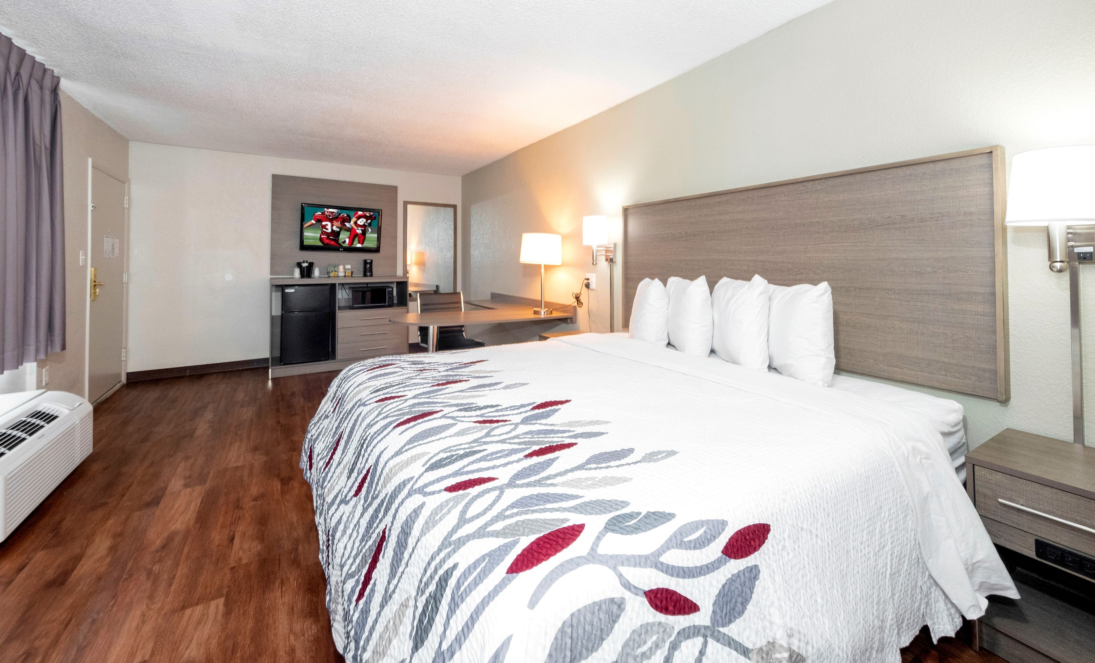 Una habitación de hotel con cama, escritorio, televisión y kitchenette.