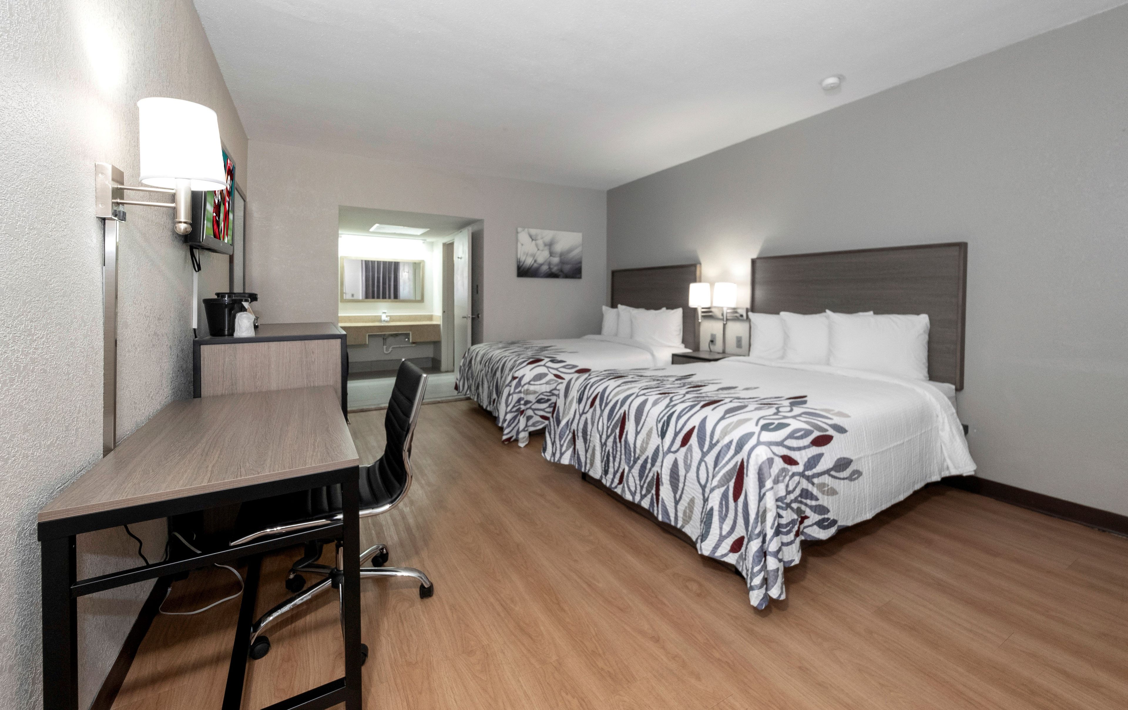 A hotel room with a desk, two beds, a bathroom, and a view of the city.