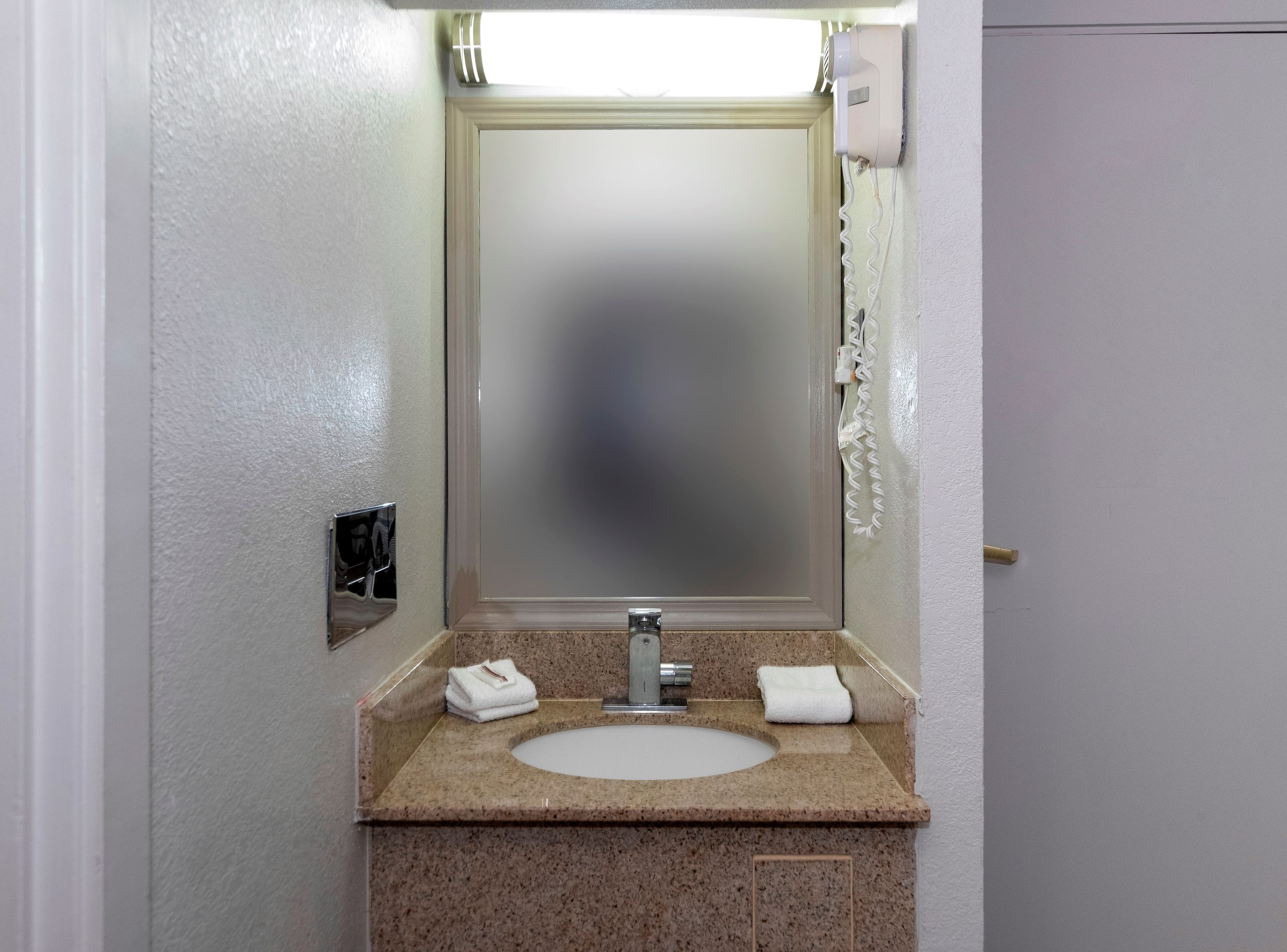 A bathroom with a sink, mirror, towel dispenser, and a telephone.
