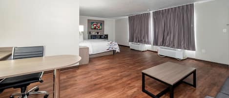 Een hotelkamer met een bed, een bureau, een stoel, een tafel, een televisie en een raam met gordijnen.