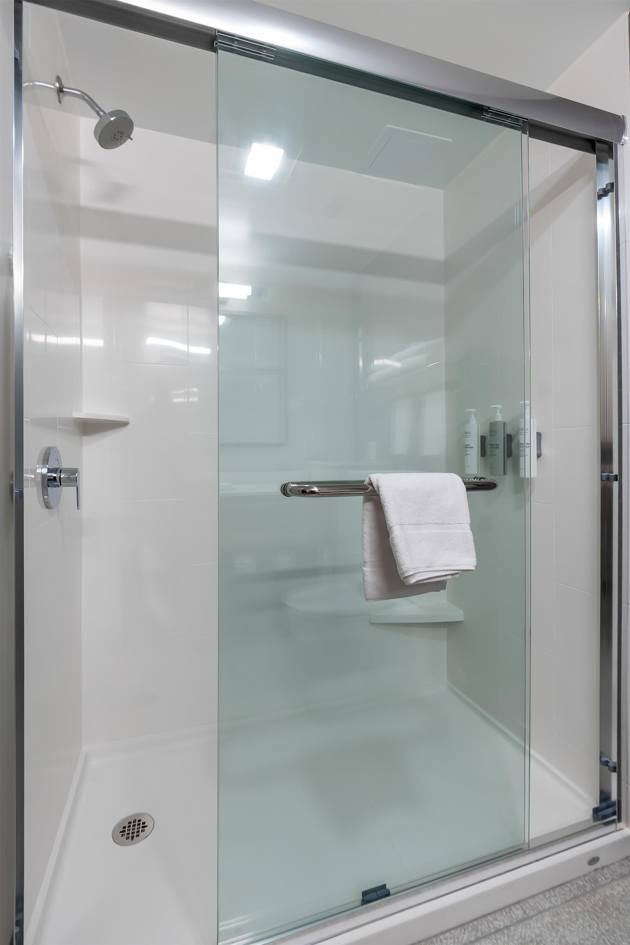 A glass-enclosed shower stall with a towel rack and a handheld showerhead.