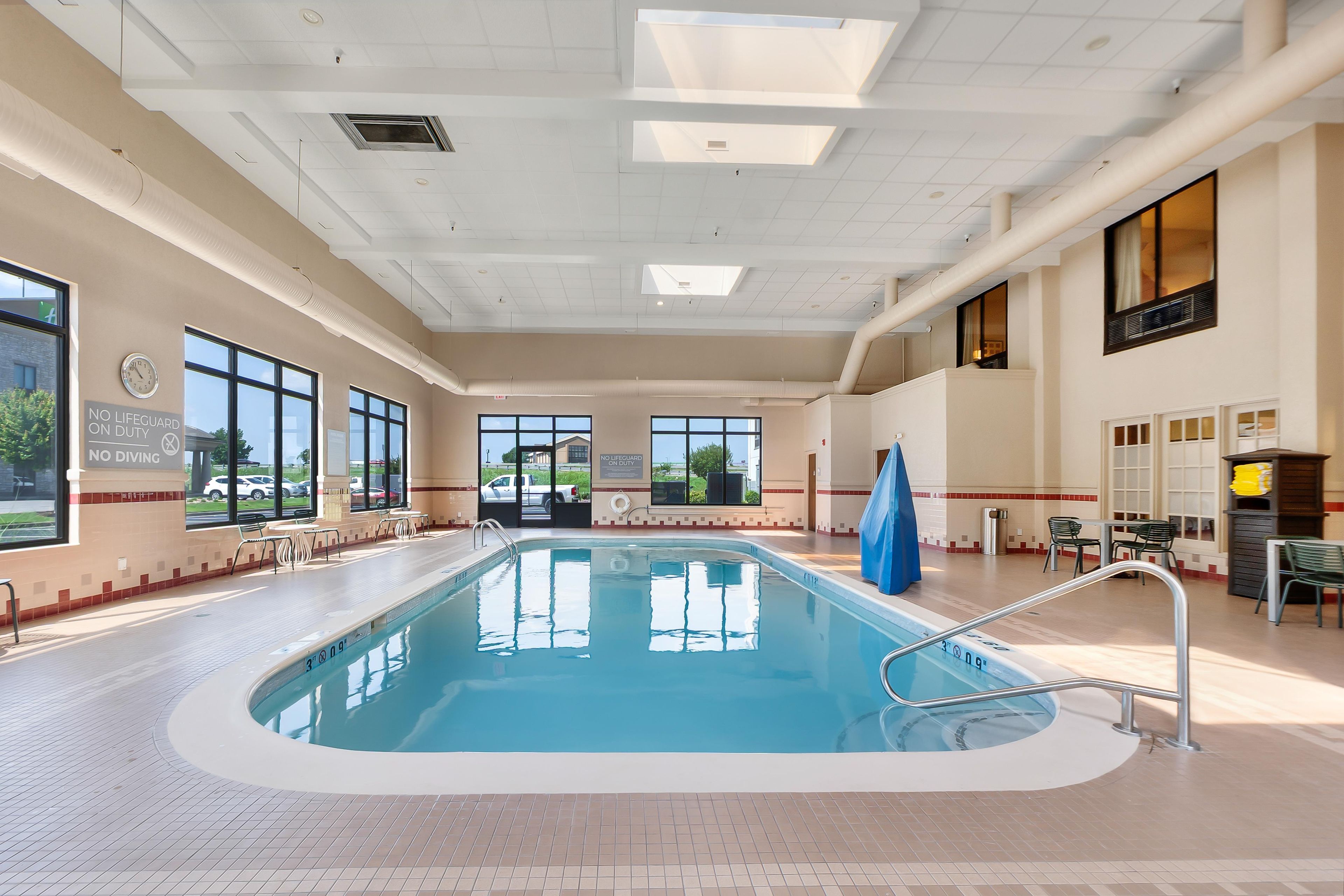 An indoor swimming pool with clear glass walls, a tiled floor, and a no lifeguard on duty sign.