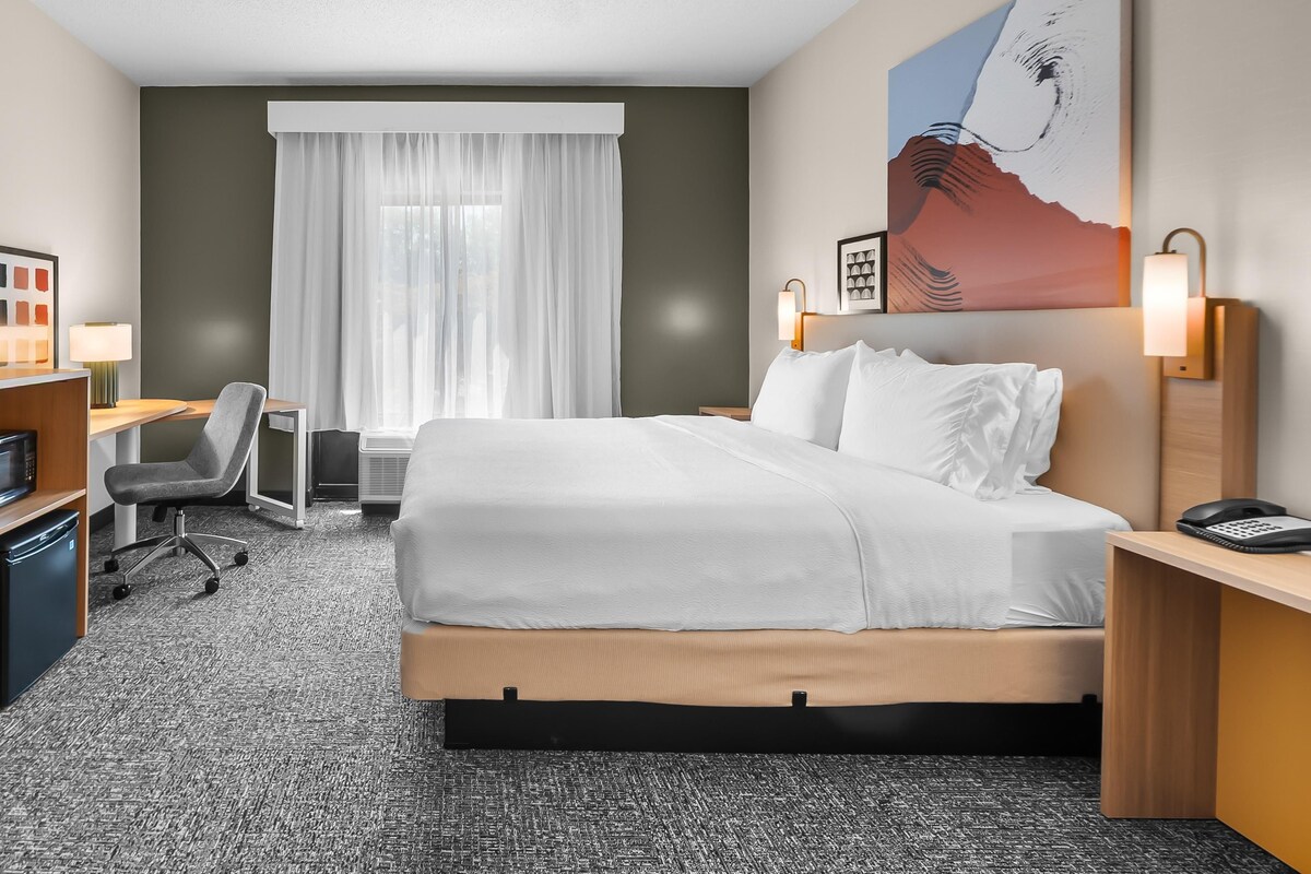 A hotel room with a bed, desk, chair, and artwork on the wall.