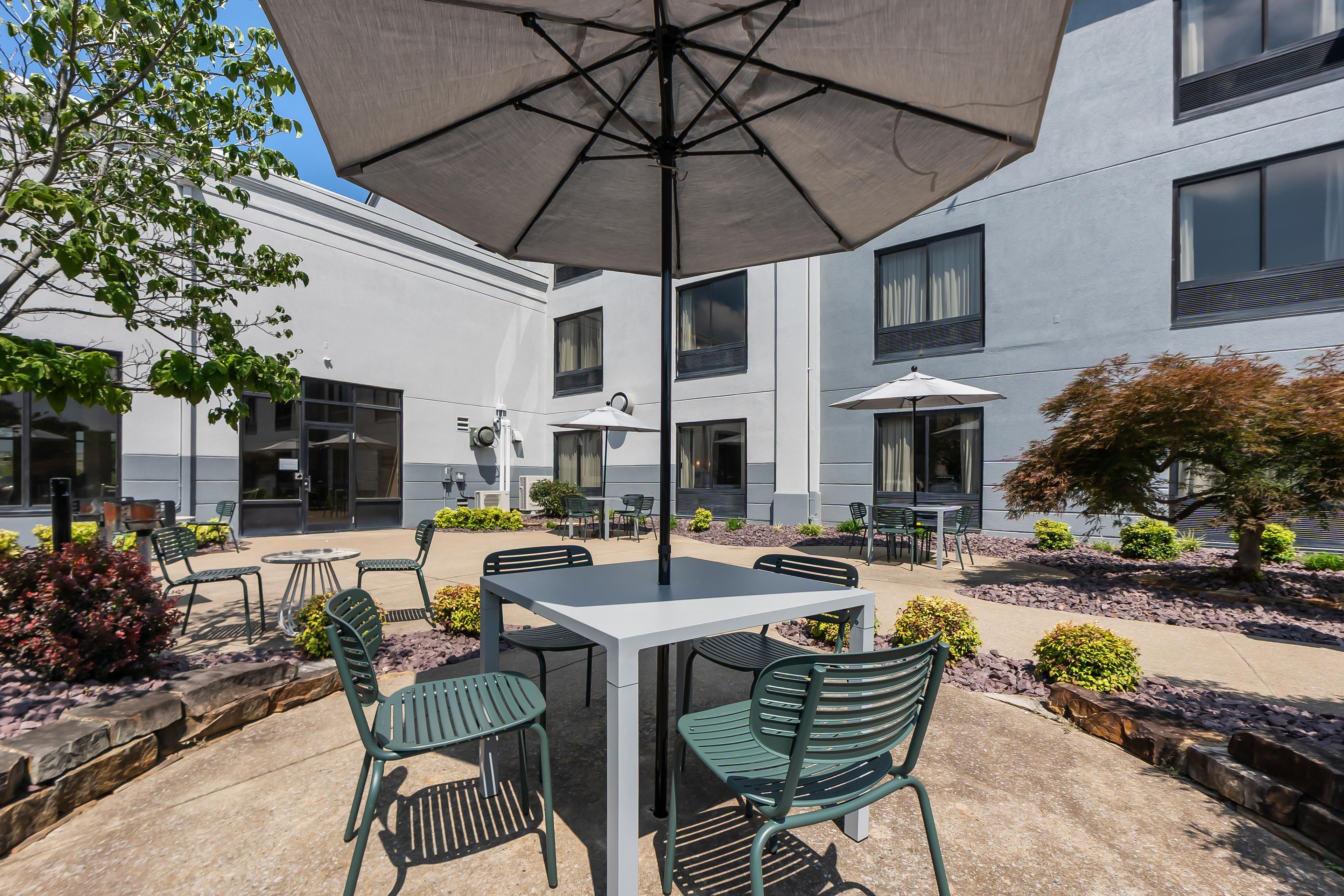 An outdoor patio with a table and chairs, surrounded by a building with multiple windows and a covered area.