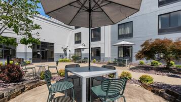An outdoor patio with a table and chairs, surrounded by a building with multiple windows and a covered area.
