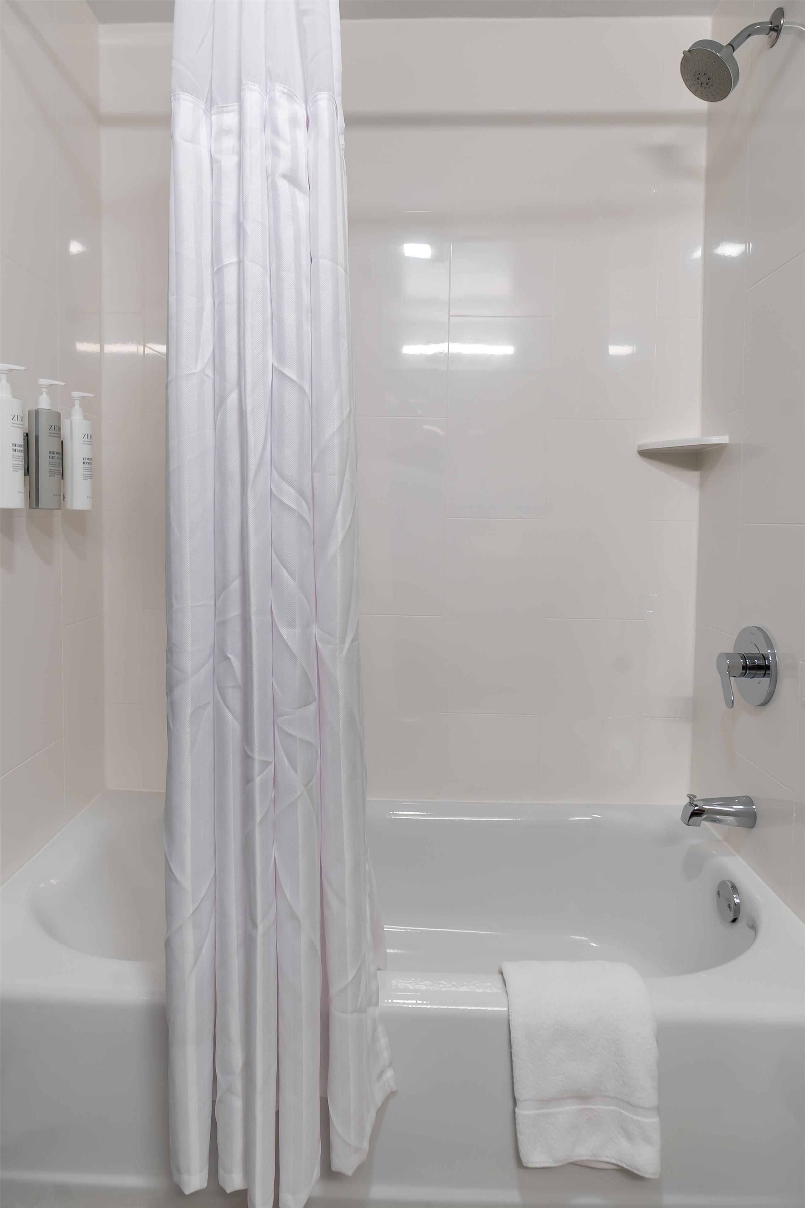 Un baño moderno con bañera, ducha y una cortina blanca.