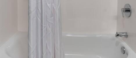 Un baño moderno con bañera, ducha y una cortina blanca.