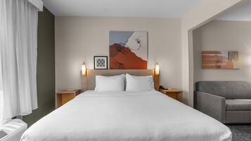 Quarto de hotel com cama grande, duas mesas de cabeceira, uma cadeira e obras de arte nas paredes.