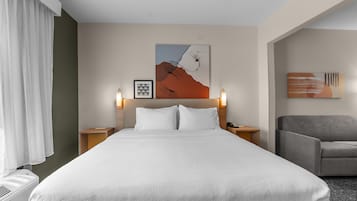 Una habitación de hotel con una cama grande, dos mesitas de noche, una silla y obras de arte en las paredes.