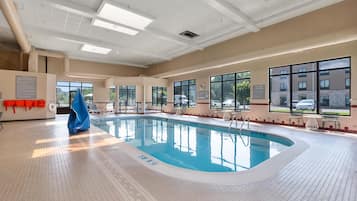 An indoor swimming pool with clear water, marked depth lines, and safety signs.