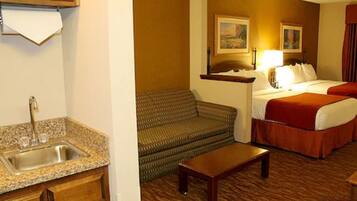 Habitación de hotel con cama, sofá, una mesita, lavamanos y un cuadro en la pared.