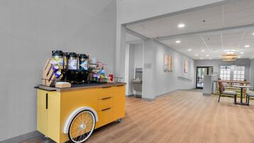 A hotel room with a yellow cart containing coffee and tea dispensers, a sink, and a bench.