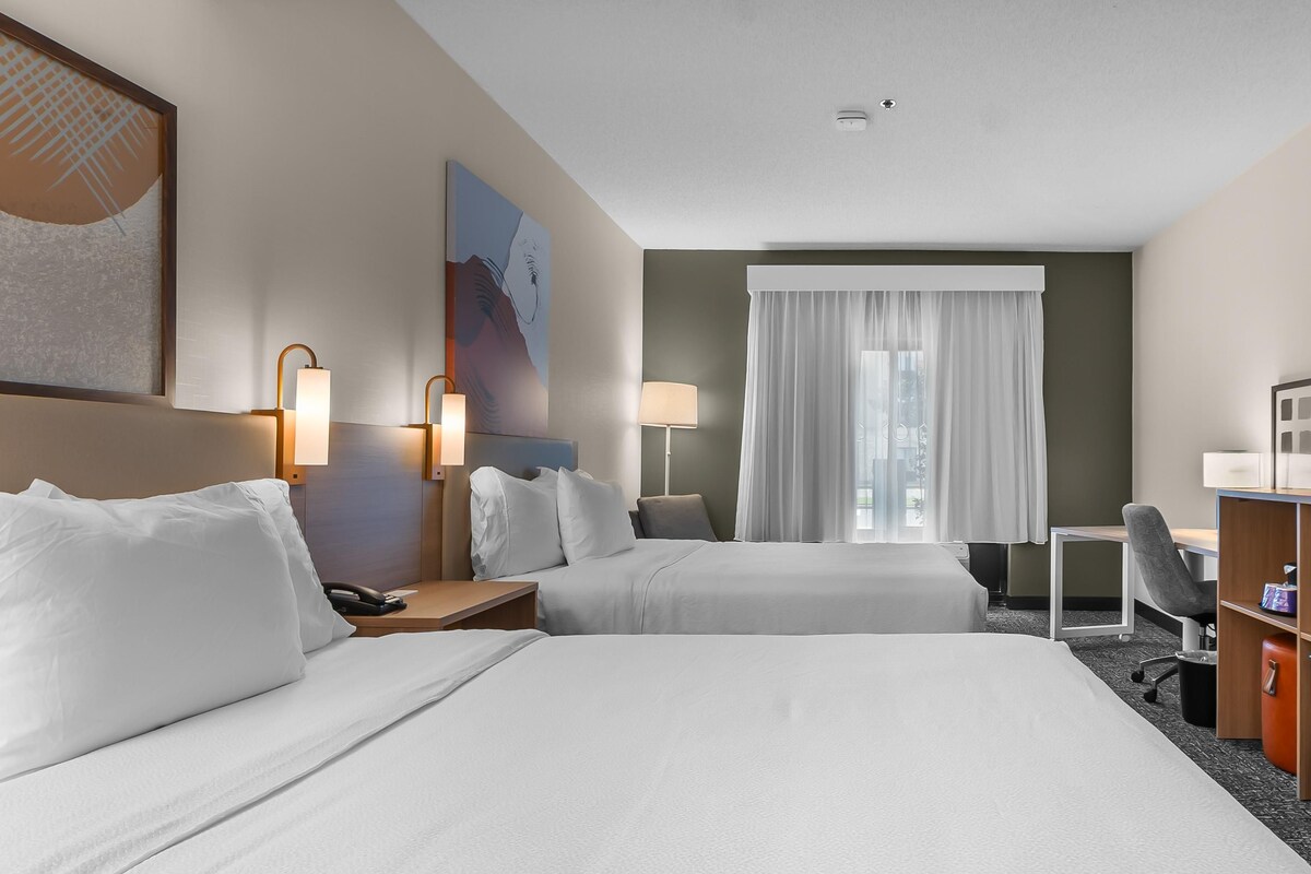 A hotel room with two beds, a desk, a chair, and a window with curtains.