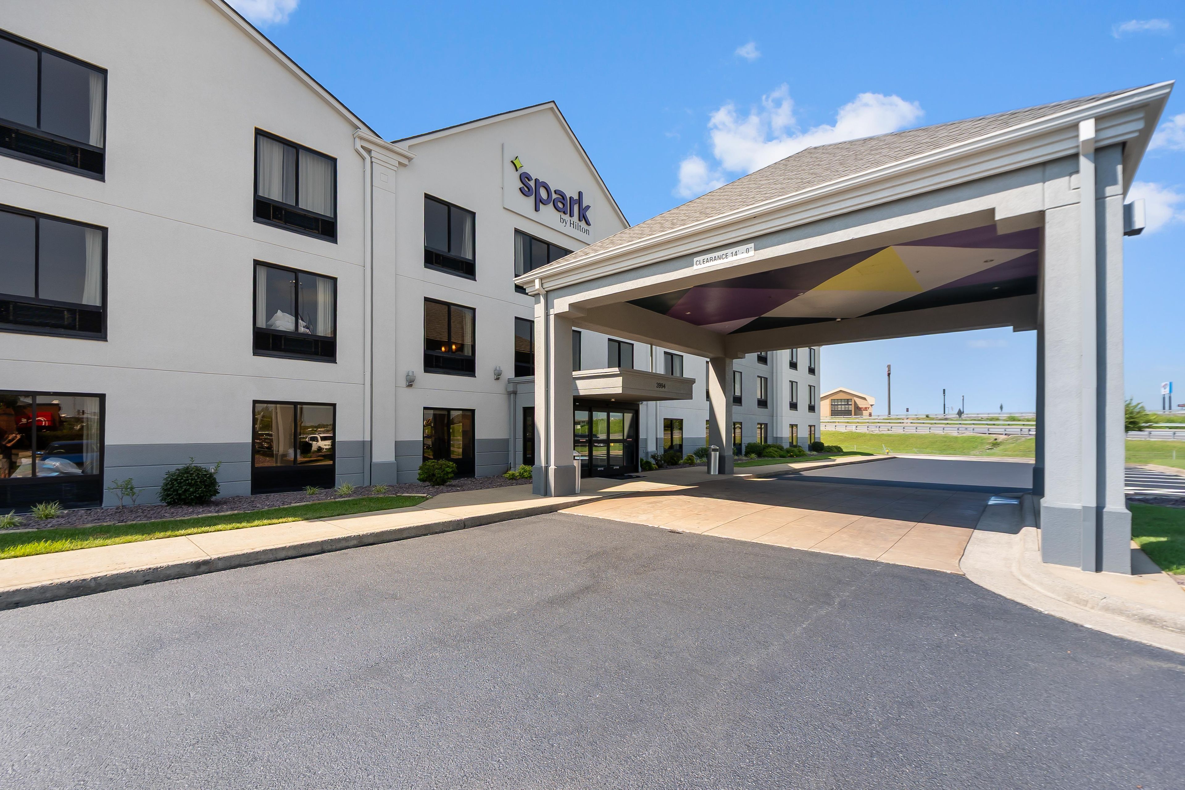 A hotel entrance with a covered parking area, a clear sky, and a building with a 'Park by Hilton' sign.