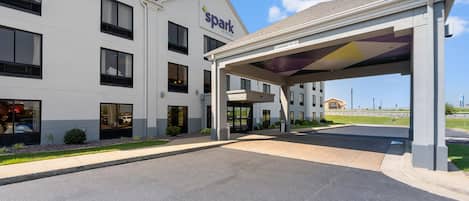 A hotel entrance with a covered parking area, a clear sky, and a building with a 'Park by Hilton' sign.