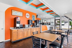 A restaurant with a counter, wooden cabinets, and a seating area with tables and chairs. - Howard Johnson by Wyndham Vero Beach / Downtown (Vero Beach)