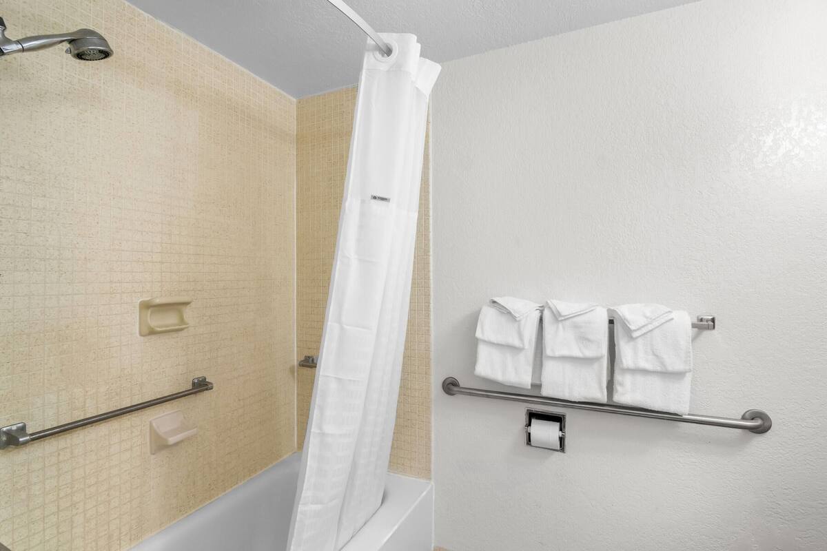 A bathroom with a bathtub, a shower curtain, a towel rack with towels, and a handrail.