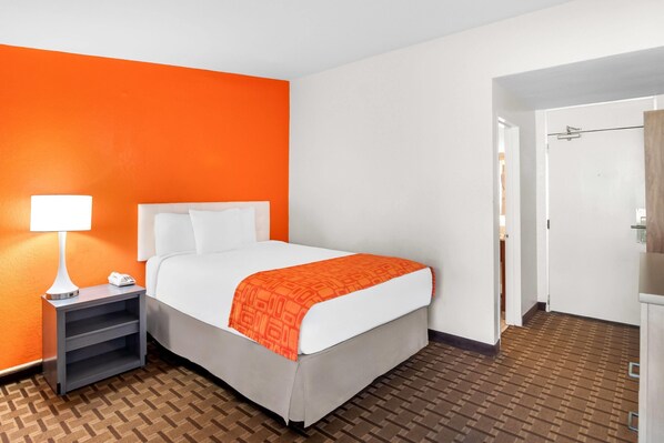 Una habitación de hotel con una cama, una mesita de noche con lámpara y un suelo estampado.