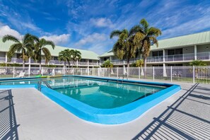 A swimming pool with a blue border, surrounded by a white fence and palm trees. - Howard Johnson by Wyndham Vero Beach / Downtown (Vero Beach)