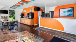 A modern lobby with a reception desk, seating area, and a display case with colorful items. - Howard Johnson by Wyndham Vero Beach / Downtown (Vero Beach)