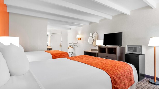A hotel room with two beds, a TV, a desk with a lamp, and a microwave. - Howard Johnson by Wyndham Vero Beach / Downtown (Vero Beach)