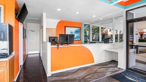 A reception area with a curved counter, a flat-screen TV, and a large window. - Howard Johnson by Wyndham Vero Beach / Downtown (Vero Beach)