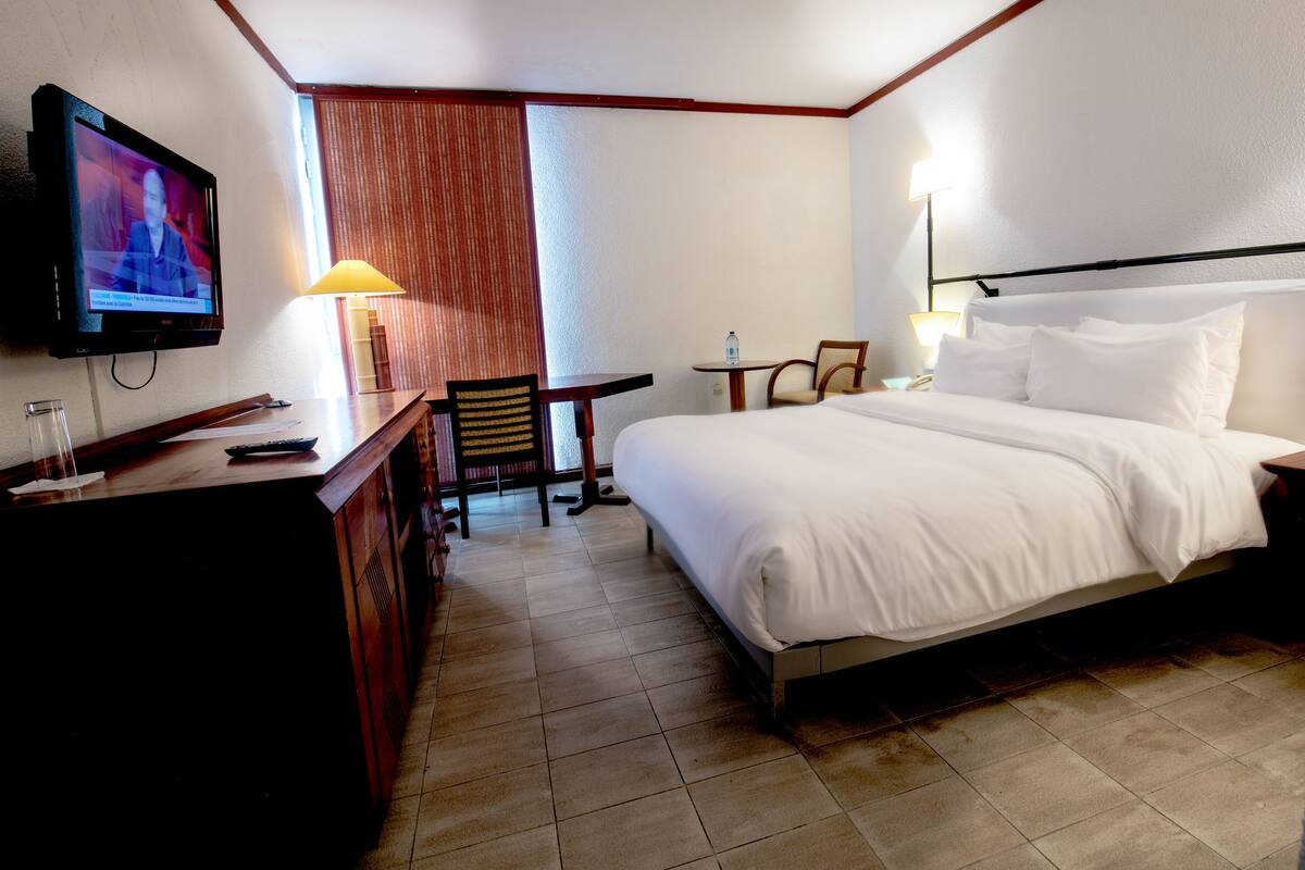 Habitación de hotel con cama, escritorio, silla, televisor y lámpara.