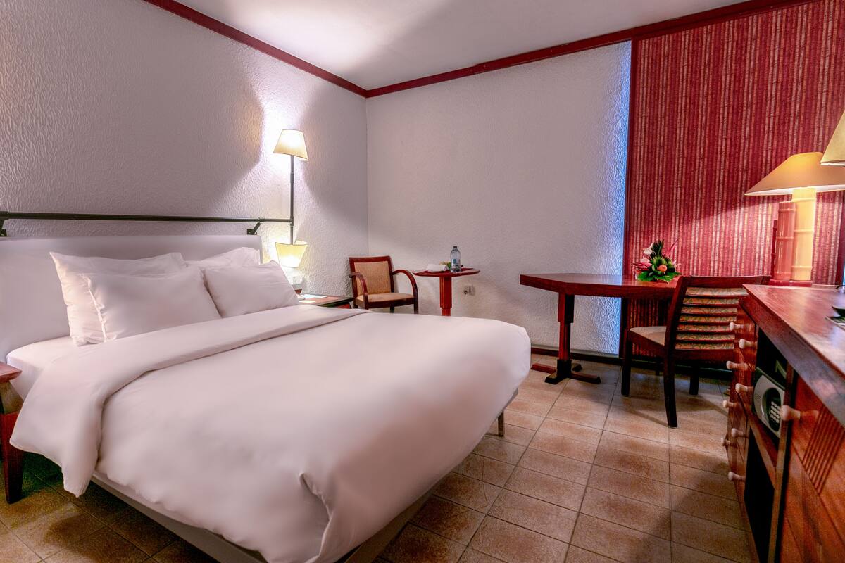 Una habitación de hotel con cama, escritorio, silla, mesita de noche y lámpara.