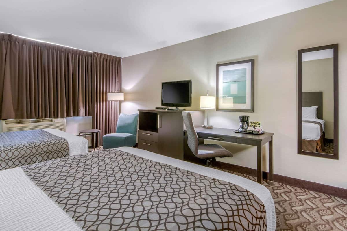 Ein Hotelzimmer mit zwei Betten, einem Schreibtisch, einem Stuhl, einem Fernseher, einer Lampe und einem Spiegel.