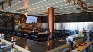 Un restaurant doté d’un bar, de plusieurs tables et de chaises. Un tableau noir fixé au mur affiche le menu, avec une liste des plats et des boissons proposés.