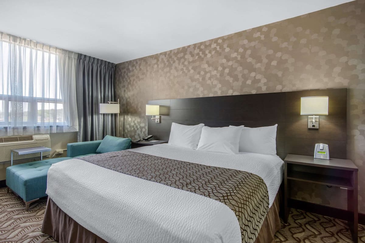 Ein Hotelzimmer mit einem großen Bett, zwei Nachttischen mit Lampen, einem kleinen Sofa und einem Fenster mit Vorhängen.