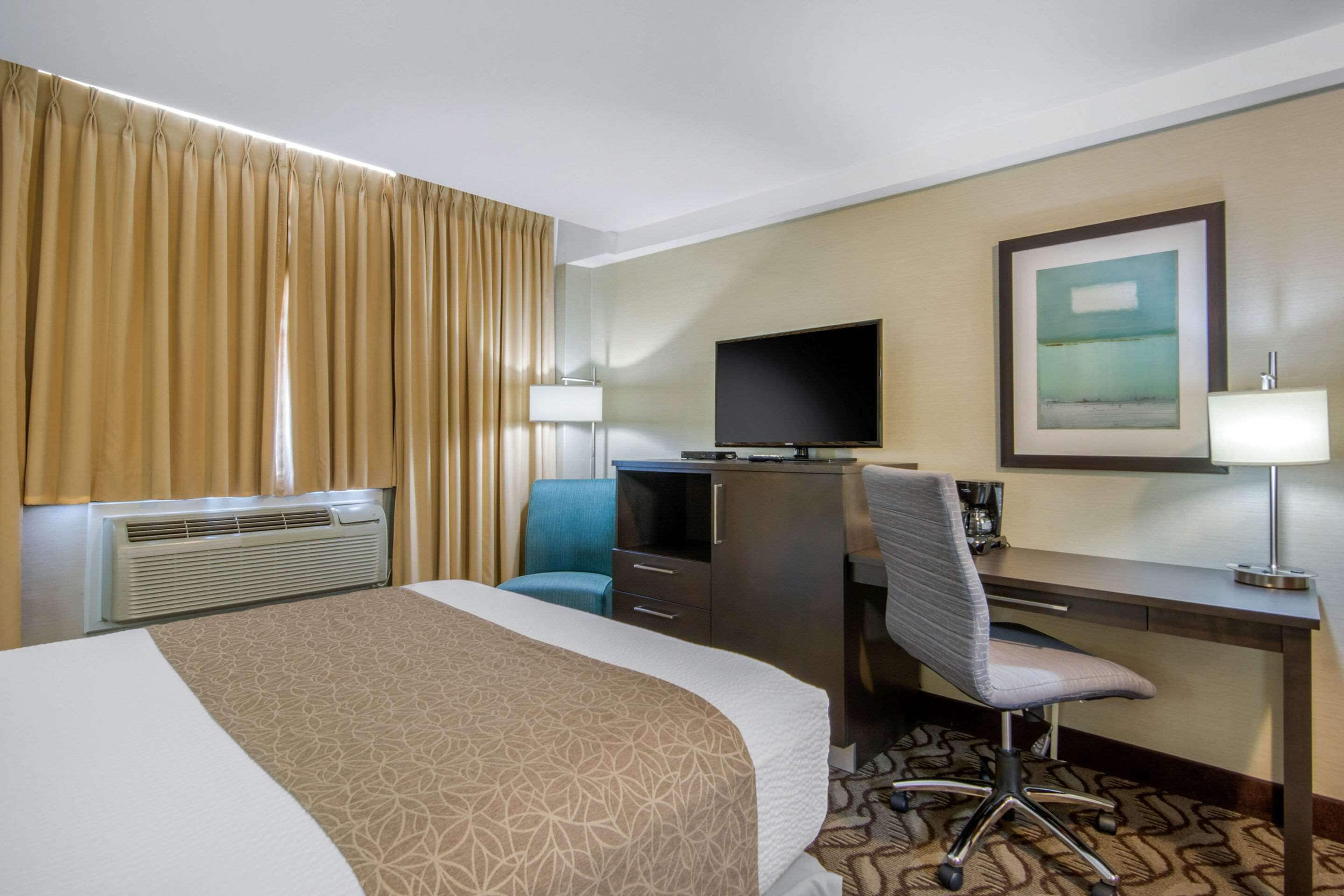 A hotel room with a bed, a desk, a chair, a television, and a painting on the wall.