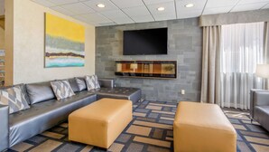 Un salon moderne avec un canapé gris, deux poufs, un téléviseur à écran plat fixé à un mur en pierre et un grand tableau abstrait.