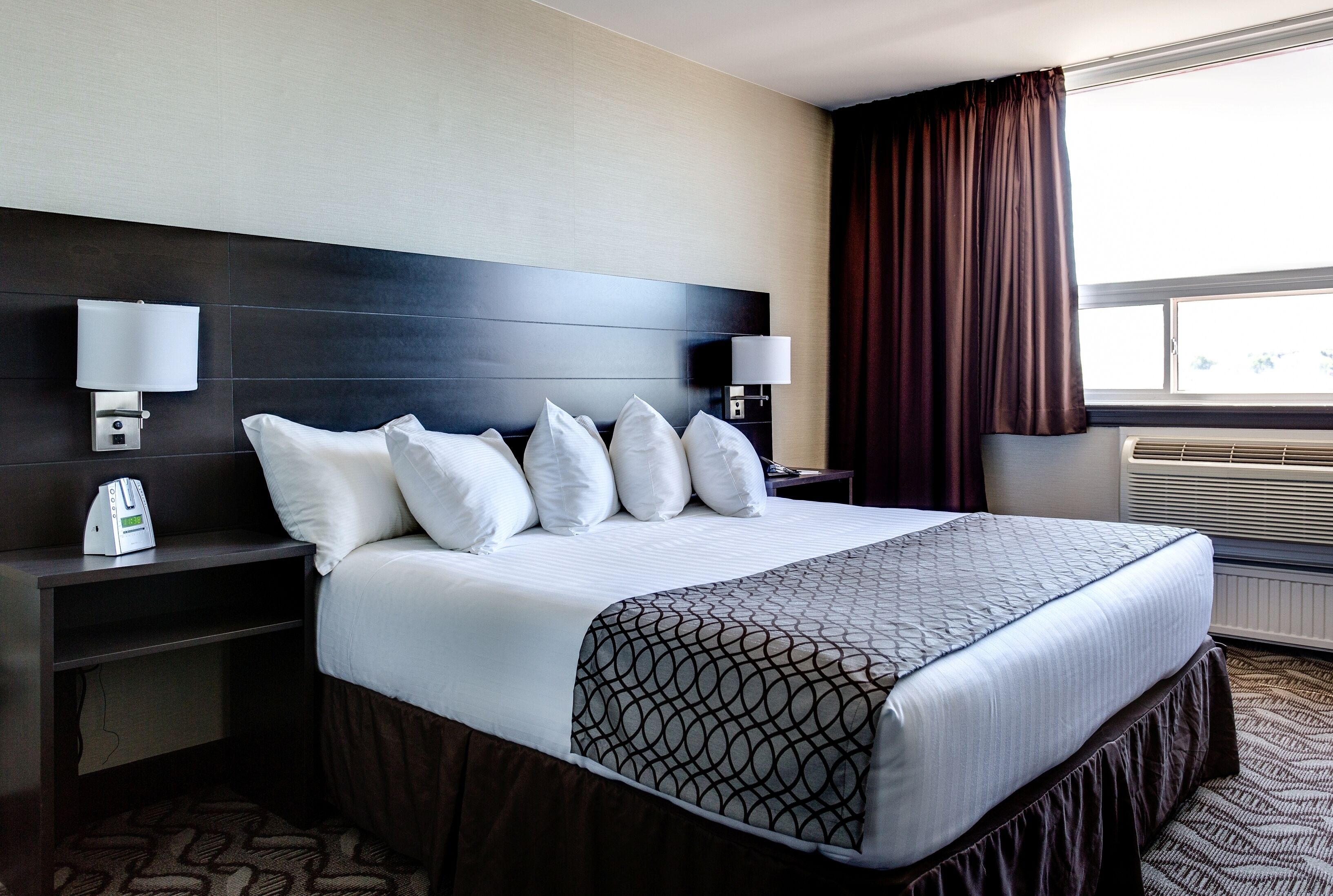 A hotel room with a large bed, two bedside tables, a wall-mounted lamp, and a window with curtains.