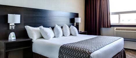 A hotel room with a large bed, two bedside tables, a wall-mounted lamp, and a window with curtains.