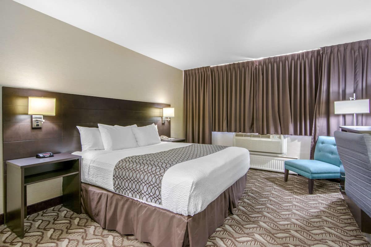Ein Hotelzimmer mit einem großen Bett, Nachttischen, einem Schreibtisch, einem Sessel und einem Fenster mit Vorhängen.