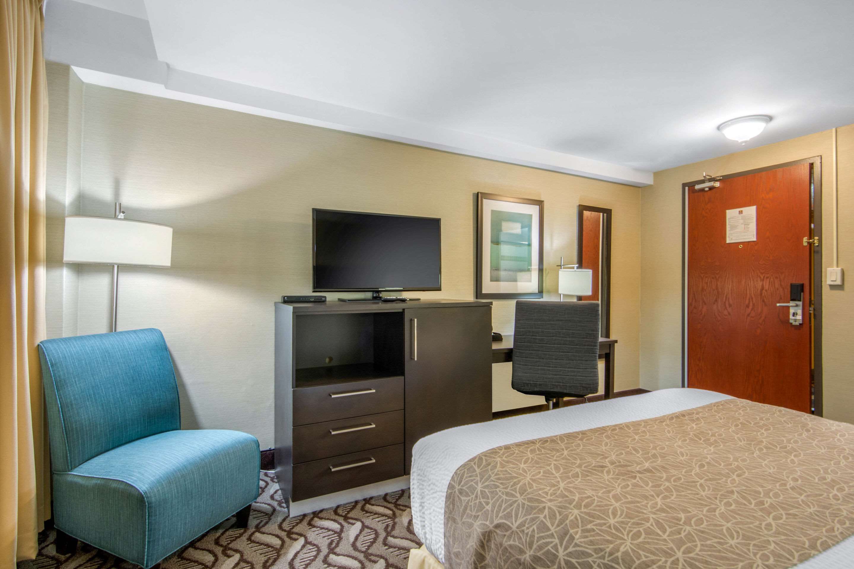 Una habitación de hotel con cama, escritorio, silla, televisor y armario.