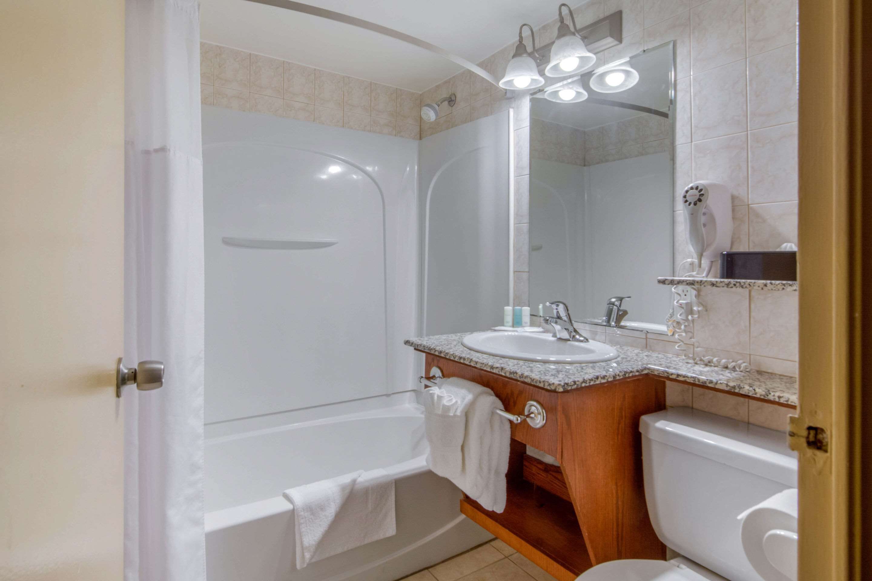 Un baño con bañera, lavamanos, espejo e inodoro.