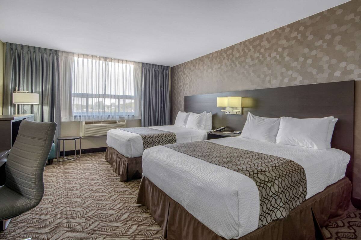 Ein Hotelzimmer mit zwei Betten, einem Schreibtisch, einem Stuhl und einem Fenster mit Vorhängen.