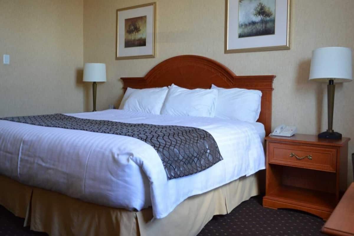 Ein Hotelzimmer mit einem Bett, einem Nachttisch, einer Lampe und zwei gerahmten Bildern an der Wand.