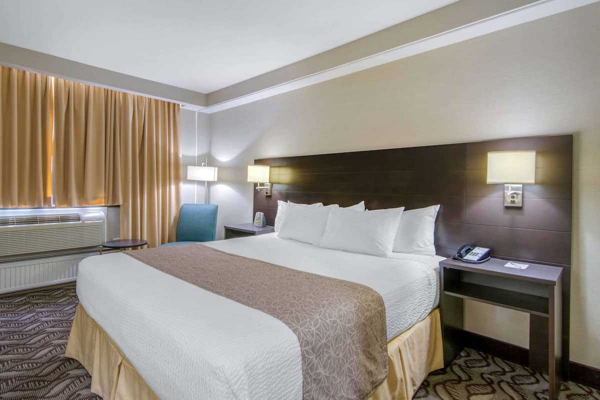Ein Hotelzimmer mit einem großen Bett, zwei Nachttischlampen, einem Telefon und einem Sessel.