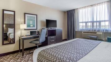Habitación de hotel con una cama grande, un escritorio con ordenador, un televisor de pantalla plana, un espejo y una ventana con cortinas.