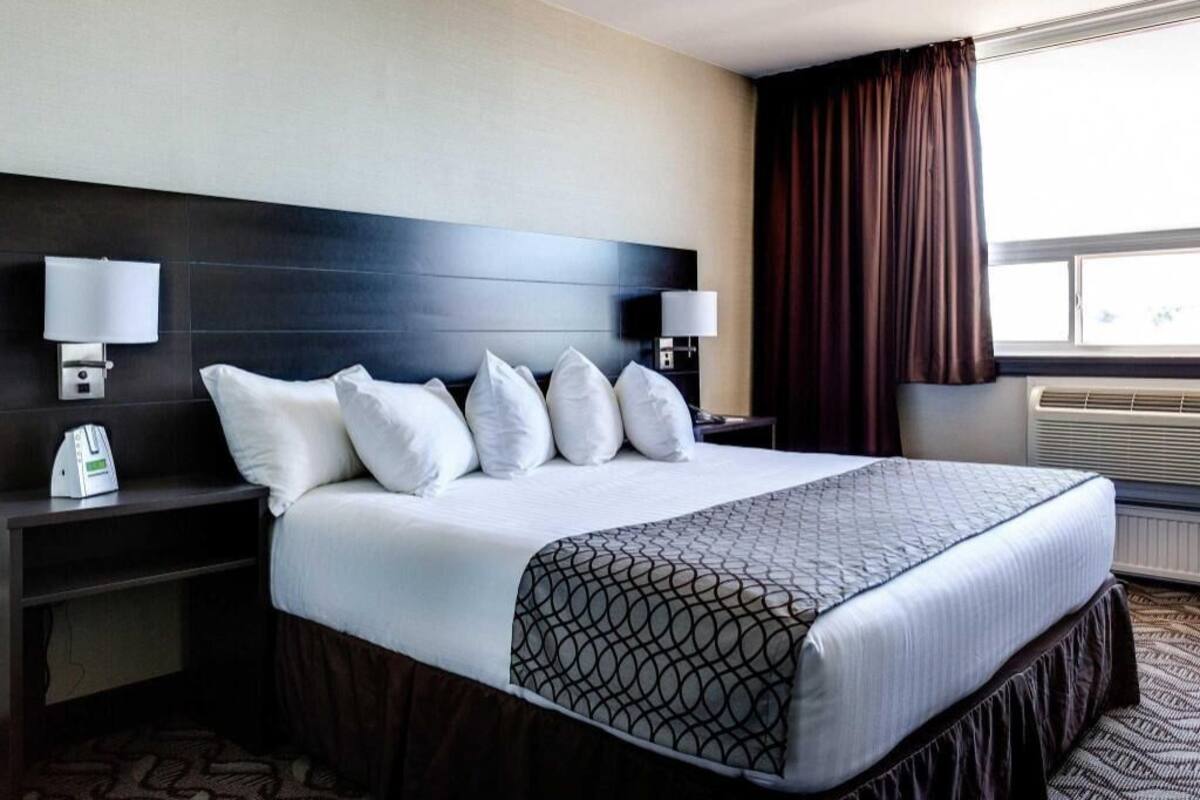Ein Hotelzimmer mit einem großen Bett, zwei Nachttischen, einer Kopfteil und einem Fenster mit Vorhängen sowie einer Klimaanlage.
